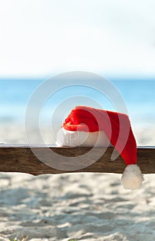 Red Santa's hat on wooden bench on the beach
