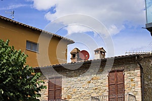 A red satellite dish placed between two chimneys on the roof of a stone house Umbria, Italy