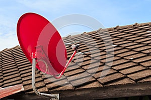 Red Satellite TV Receiver Dish on the Old Tiles Roof