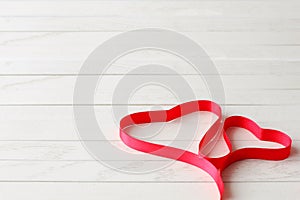 Red Satin Ribbon in Shape of Two Hearts on Wooden Background