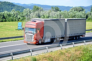 Red Scania truck coupled with trailer drived on slovak D1 highway in countryside.
