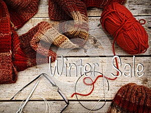 Red scarf and hat near knitting needles and woolen threads on wooden background. Winter and autumn warm clothing