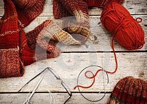 Red scarf and hat near knitting needles and woolen threads on wooden background. Winter and autumn warm clothing, top view.