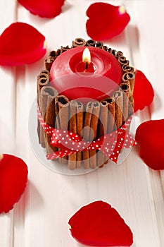 Red scented candle decorated with cinnamon sticks. Rose petals a