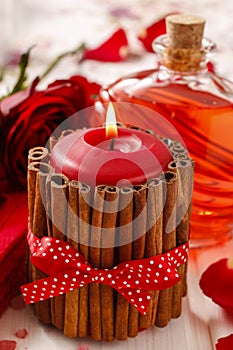 Red scented candle decorated with cinnamon sticks. Rose petals a