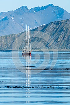 Red schooner motoring into bay past mountains