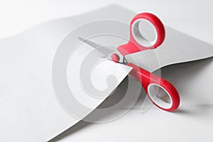 Red scissors cutting paper on white wooden background, closeup