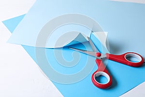 Red scissors and light blue paper on white background