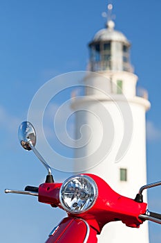 Red scooter parked near a lighthouse.