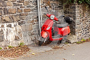 Red scooter parked on the street in front of a wall