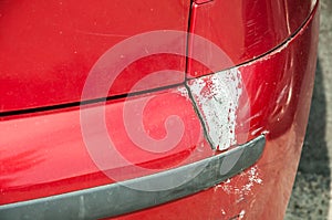 Red scratched car with damaged paint in crash accident or parking lot and dented damage of bumper metal body from collision