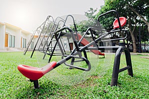 Red seesaw in the playground. Playground equipment for children to play. Plastic seesaw or teeter-totter, swing, and slide at