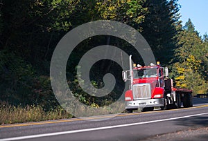 Red semi truck with flat bed trailer on forest road