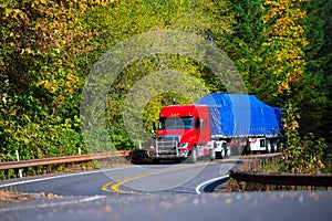 Red semi truck flat bed trailer on winding autumn highway