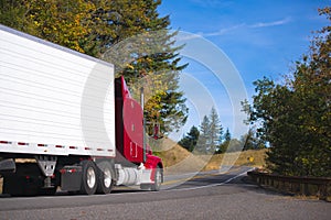 Red semi truck rig and trailer on autumn convoluted highway