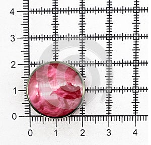 Red sewing button with a beautiful pattern on a square measuring ruler