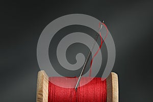 Red sewing thread with needle on dark background, closeup