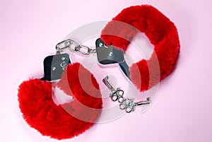 Red sexy fluffy handcuffs with keys on a pink background