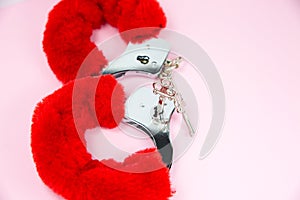 Red sexy fluffy handcuffs with keys on a pink background