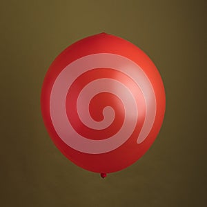 Red Shiny Balloon Against An Olive Green Background