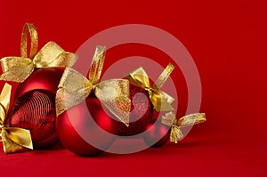 Red shiny different christmas balls with gold shimmer bow on bright deep red background, closeup, copy space. New year background.