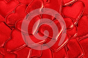 Red shiny fabric hearts arranged randomly. Background