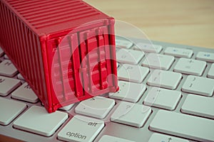 Red shipping cargo container on white keyboard computer and wooden table background. E-commerce or online shopping, logistic