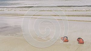 Red shoes on the sandy beach with sea water and waves