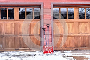 Red shovels on snowy driveway against wall and wooden garage doors of home