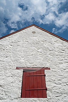 Red shutter, antique hinges, and pointed piqued roof on old farm.