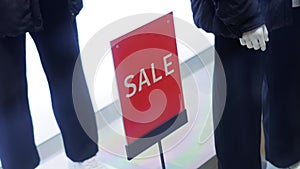 Red sign with the inscription sale in a clothing store on the background of mannequins with modern stylish clothes