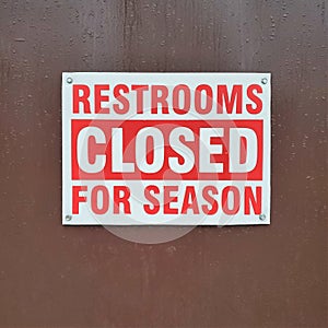 Red sign `Restrooms Closed for Season` posted on wood door