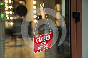 Red sign with words Closed Due To Covid-19 hanging on glass door