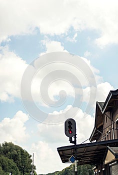 Red signal light at train station with blue cloudy sky.