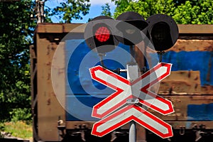 Red signal of semaphore and stop sign in front of railroad crossing with train passing