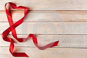 Red silk ribbon in shape of a heart on a wooden background. Valentine& x27;s day concept. Place for text.