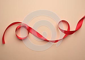 red silk ribbon twisted on a beige background, festive backdrop