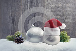 Christmas balls with Santa hat and fir twigs in the snow