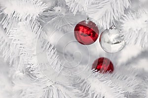 Red and silver ornament balls on white christmas tree branches.