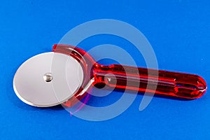 A red plastic pizza cutter sits on a blue surface