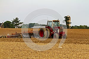 A red six wheel International 1586 tractor with cabin is plowing a blank agricultural field