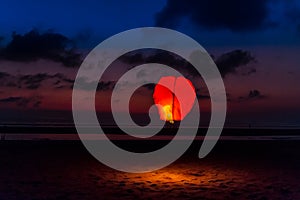 A red sky lantern floating at dusk a little after sunset on Seminyak Beach above the sand in Bali, Indonesia, Asia