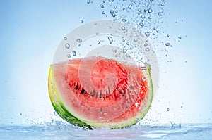 Red slice of watermelon in a splash of water on a blue background