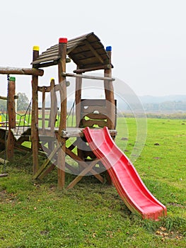 Red slide from wooden crawl construction on modern kids playground