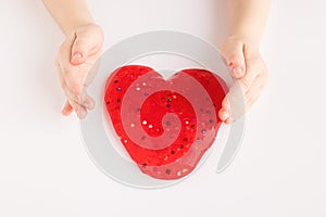 Red slime in heart shape in kid hands. Kid hands playing slime toy on white background. Love and valentines day concept