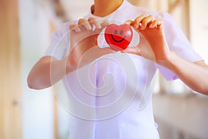 Red smiling heart held by female nurse`s hand, representing giving effort high quality service mind to patient. Professional, Spec