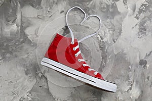 Red sneaker and white shoe lace in shape of heart on grey stone table, top view