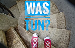 Red sneakers on spiral staircase when going downhill with inscription in german Was tun? in english What to do?