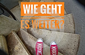 Red sneakers on spiral staircase when going downhill and the inscription in german Wie geht es weiter? in english Whats next?