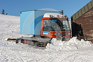 Red snowcat, fully tracked vehicle designed to move on snow in front of ski lodge in krkonose mountains, Czech Republic